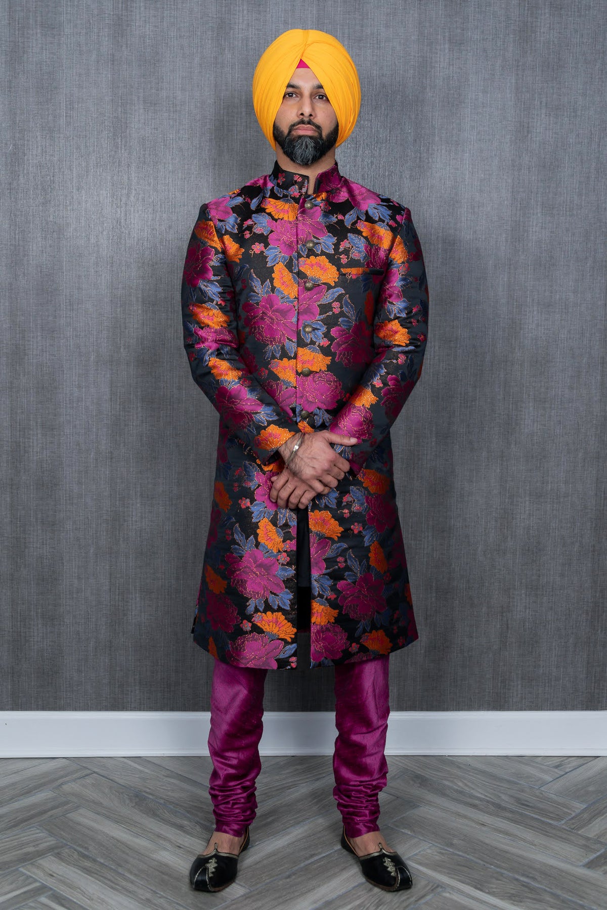 Front view- man wearing a Colorful floral sherwani jacket with accents of black purple and orange paired with purple pajama pants and a yellow turban