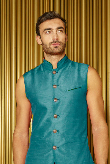 Man wearing a teal vest against a gold curtain background