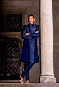 Man wearing ARUN Silk Sherwani Jacket in Navy with matching navy raw silk pajama pants standing next to a pillar.