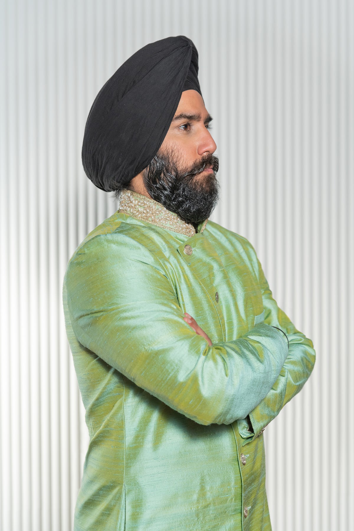 Side view- man wearing an Asymmetrical Sherwani Jacket in Sage Green with pearl collar detailing standing in front of a white background 