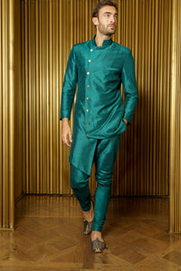 Front view- man wearing an Asymmetrical Sherwani Jacket in Evergreen paired with matching pajama pants standing in front of a gold background 