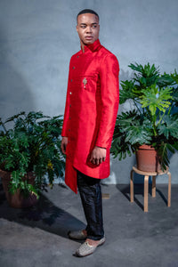 Side view- man wearing an Asymmetrical Sherwani Jacket in Red paired with black pajama pants standing in front of a blue background 