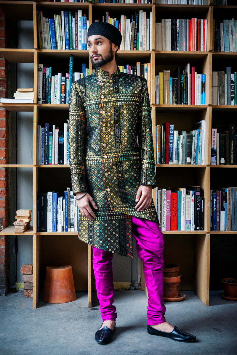Geometric sherwani and fuschia pajama pants standing in front of a bookshelf