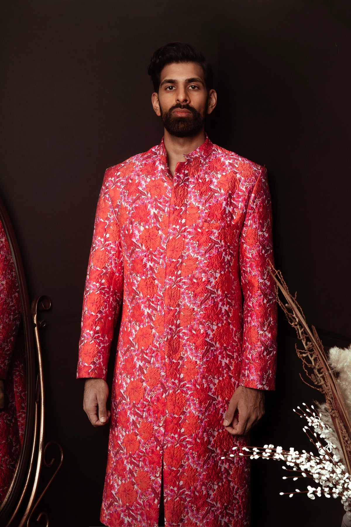 Front view- Man wearing red and pink floral sherwani in front of a brown background 