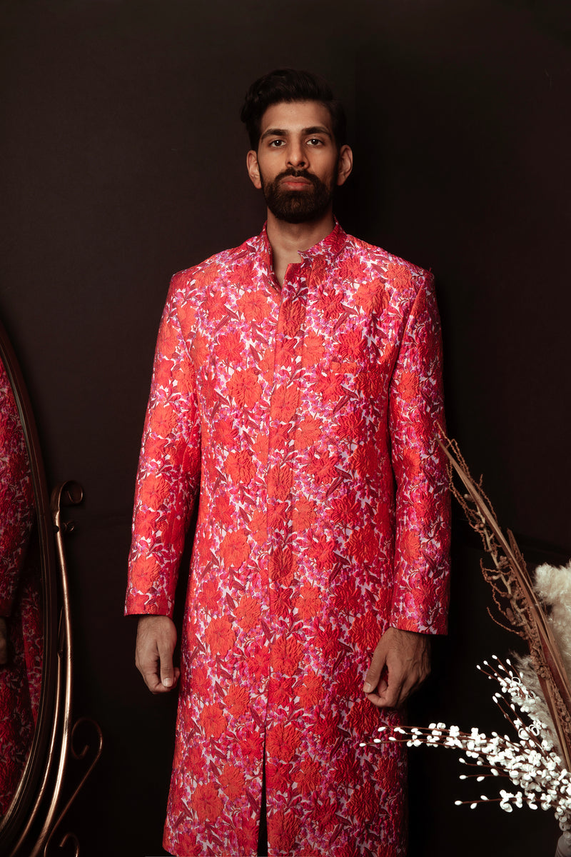 Front view- Man wearing red and pink floral sherwani in front of a brown background 