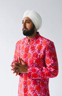 Side view- man wearing a red floral sherwani with a white turban standing in front of a white background 
