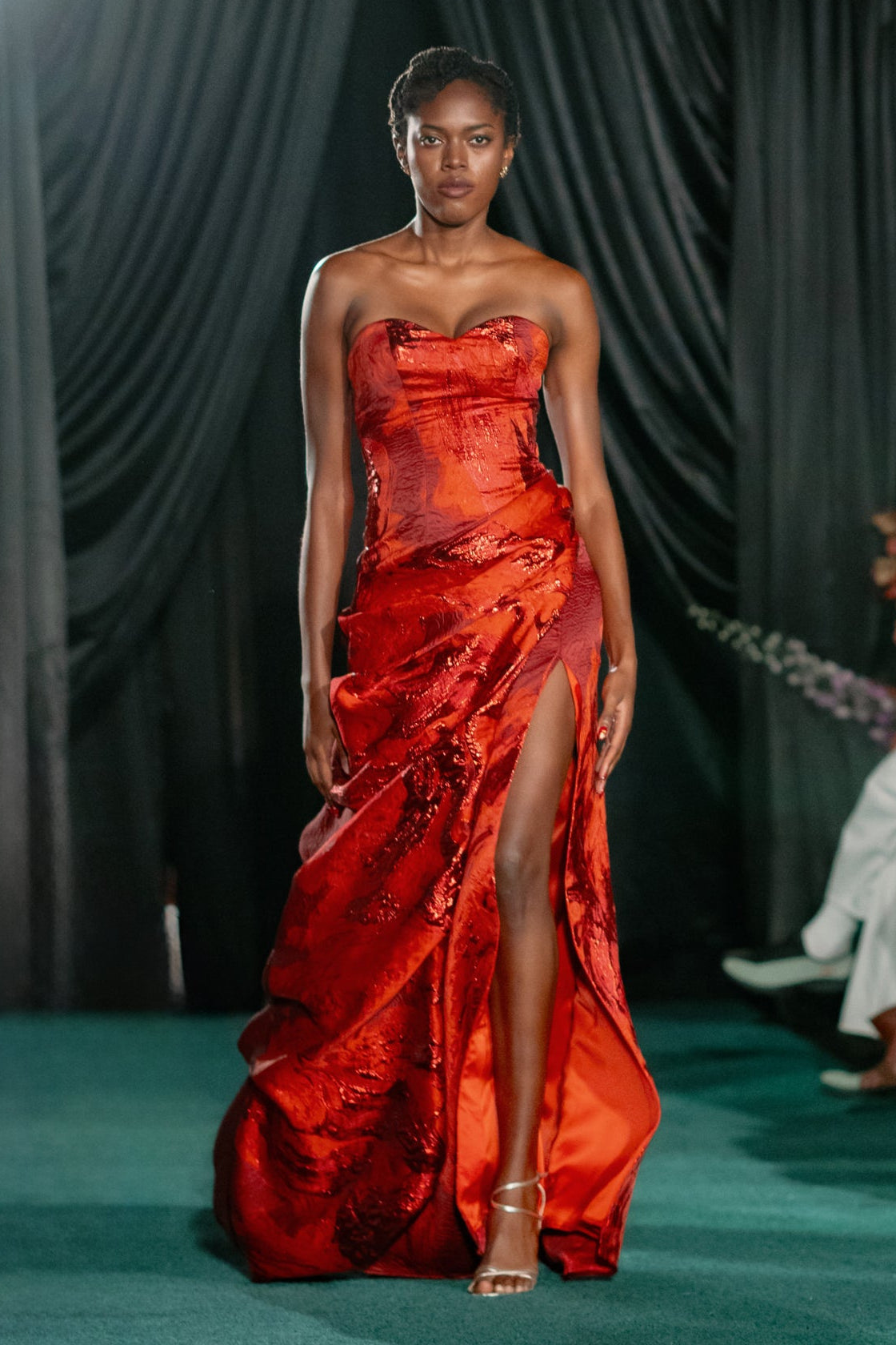 Model wearing a red strapless gown with a high slit on a runway.