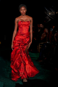 Model wearing a red strapless gown at a fashion event.