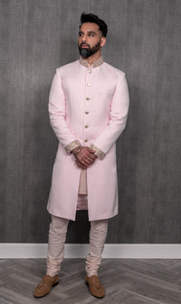 Front-facing view- man wearing a light pink sherwani jacket with pearl cuffs and collar with matching pajama pants in front of simple gray background