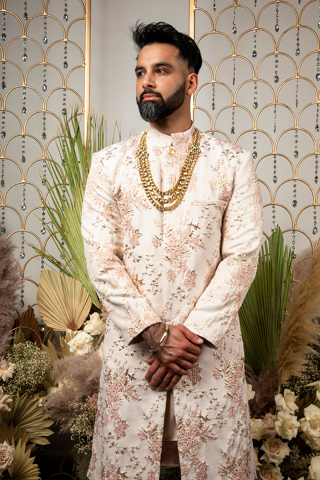 front view- man wearing PARK Blush-Gold Floral Jacquard Sherwani Jacket in front of a gold and floral background with layered necklaces