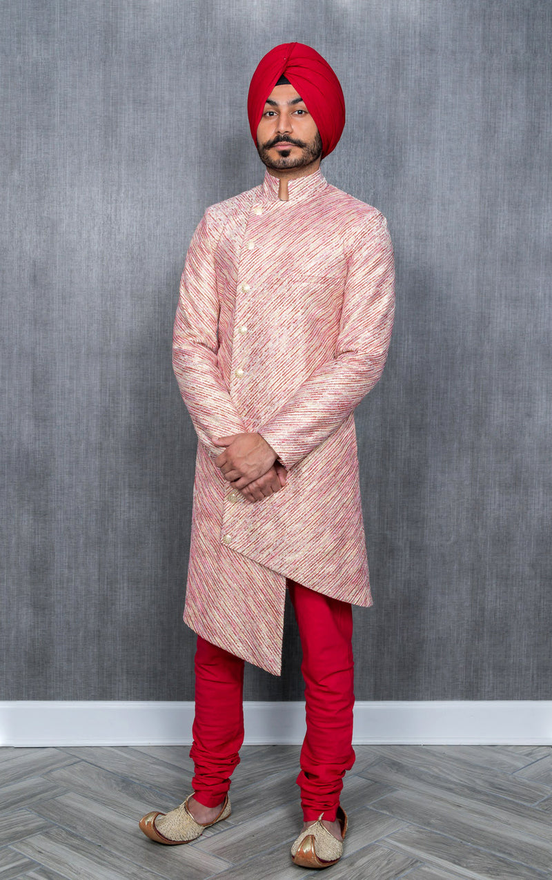Front view- man wearing a red and gold striped sherwani with red pajama pant and red turban in front of a grey background 