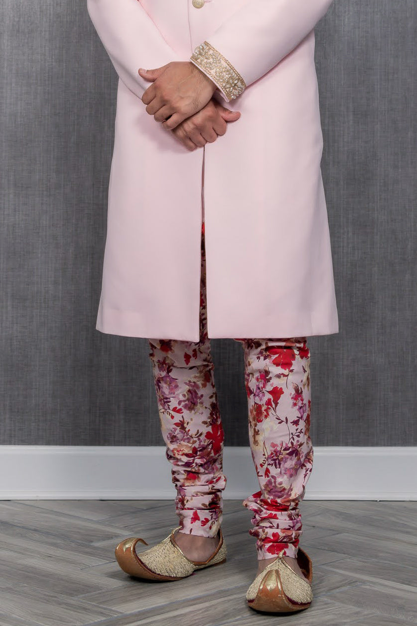 front view of man wearing VIHAAN red floral pajama pants with a light pink sherwani and gold shoes in front of a gray background