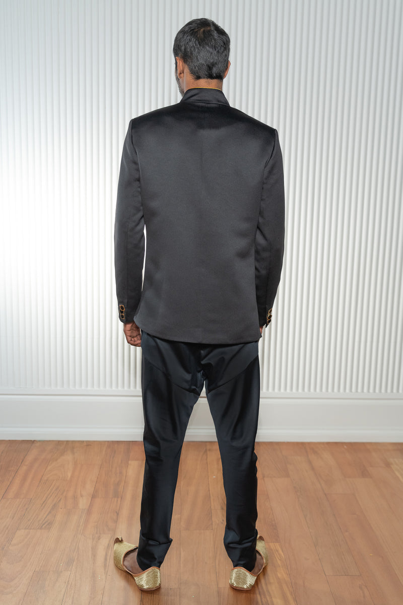 Back view- man wearing a black asymmetrical jodhpuri jacket paired with black pajama pants 