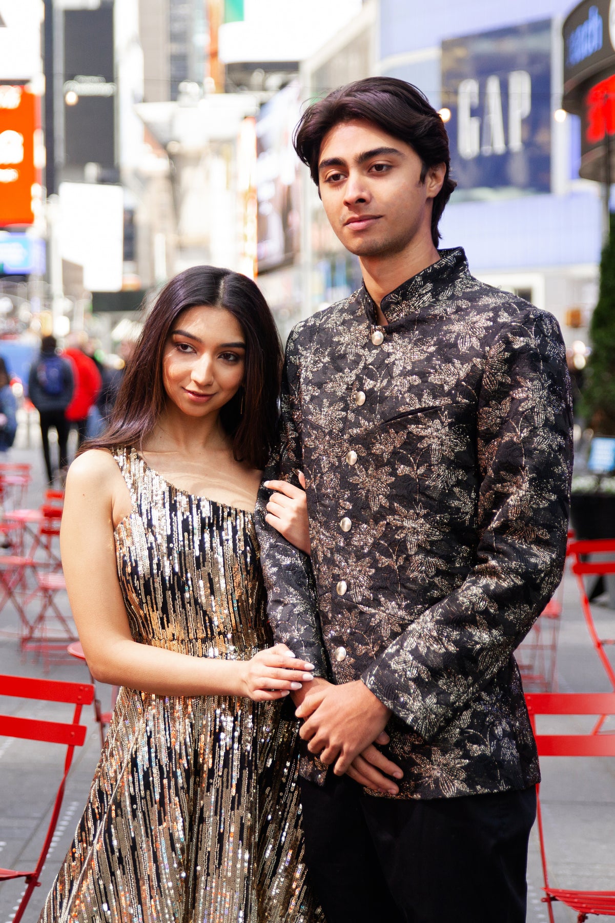 Man dressed in black and gold jodhpuri jacket with floral jacquard design next to a woman in a black and gold sequin dress
