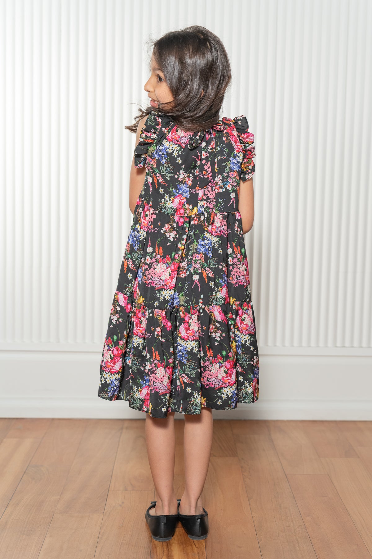 Satya wearing the Paloma Tiered Dress in black with vibrant florals - Back View - Harleen Kaur